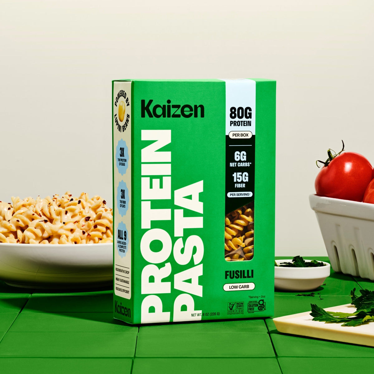 Kaizen Protein Pasta Fusilli box beside a bowl of cooked fusilli and fresh tomatoes