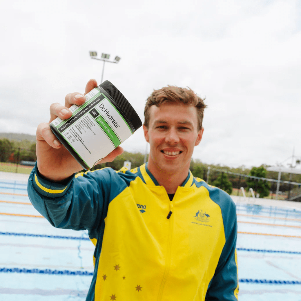 Man in yellow and blue jacket holding Dr. Hydrate Green Apple Jar - 30 Serves near an outdoor swimming pool