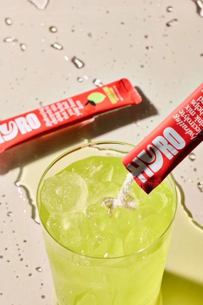 Hyro Single Stick electrolyte powder being poured into a glass of ice with green drink from Hyro functional low carb collection.
