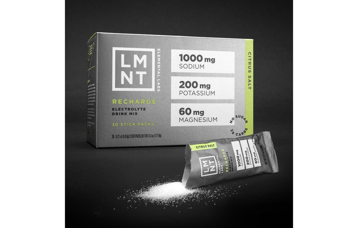 Box of LMNT Citrus Salt Electrolyte Mix with three individual packets and spilled white powder on black surface.