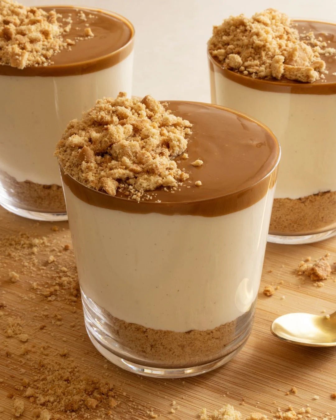 Three dessert glasses with creamy layers and biscuit crumbs, styled to promote Organic Whey Protein - Vanilla - 750g