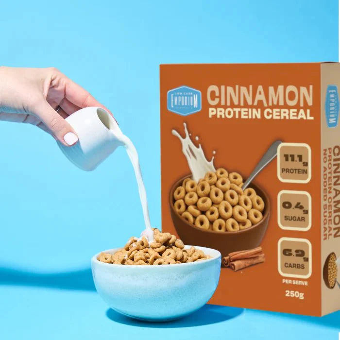 Hand pouring milk into bowl of Protein Cereal - Cinnamon Flavour - 250g by Low Carb Emporium against blue background
