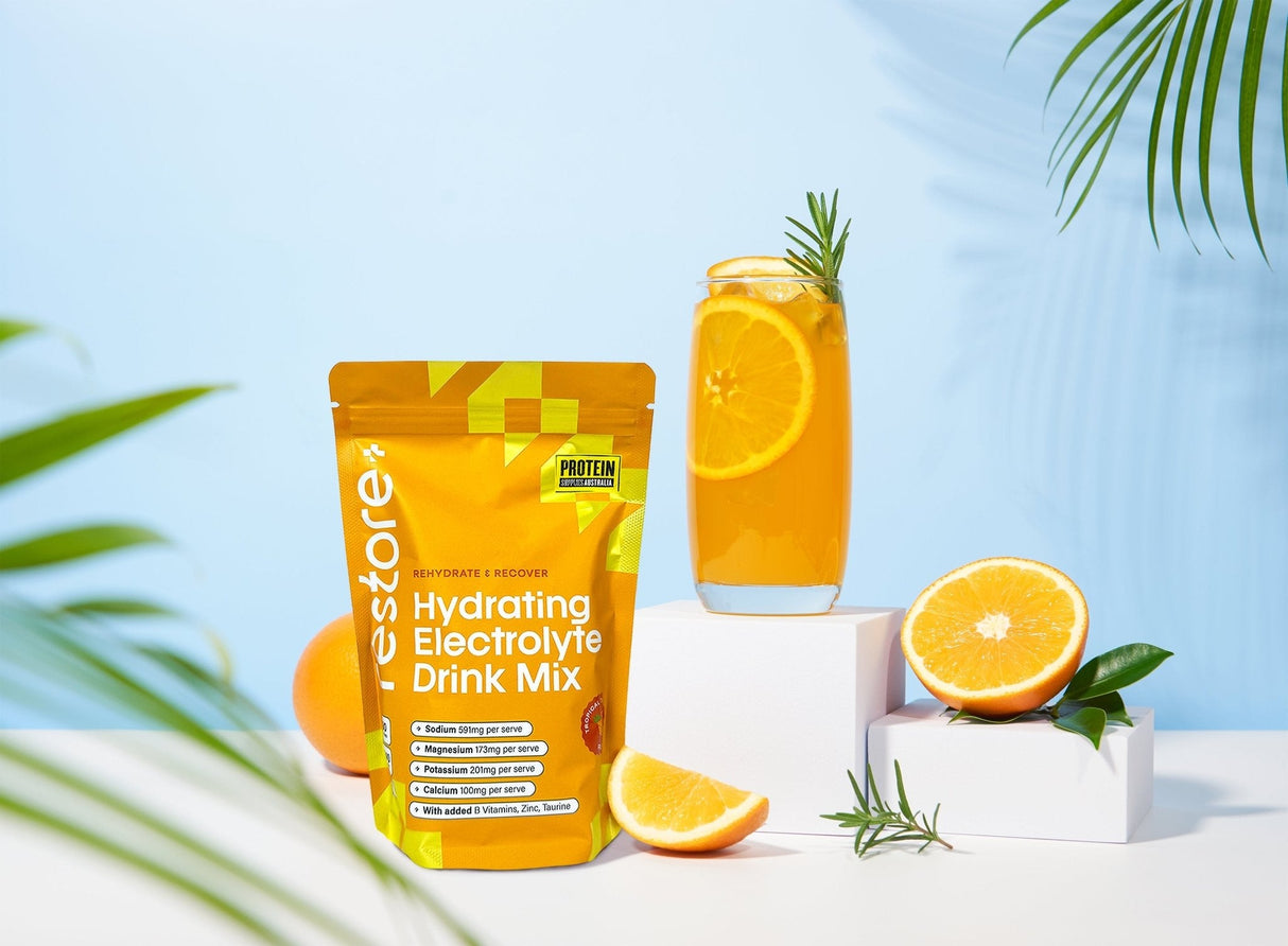 Restore Electrolyte Drink Mix Tropical Twist 240g by Protein Supplies Australia with tropical orange drink and fresh fruit display