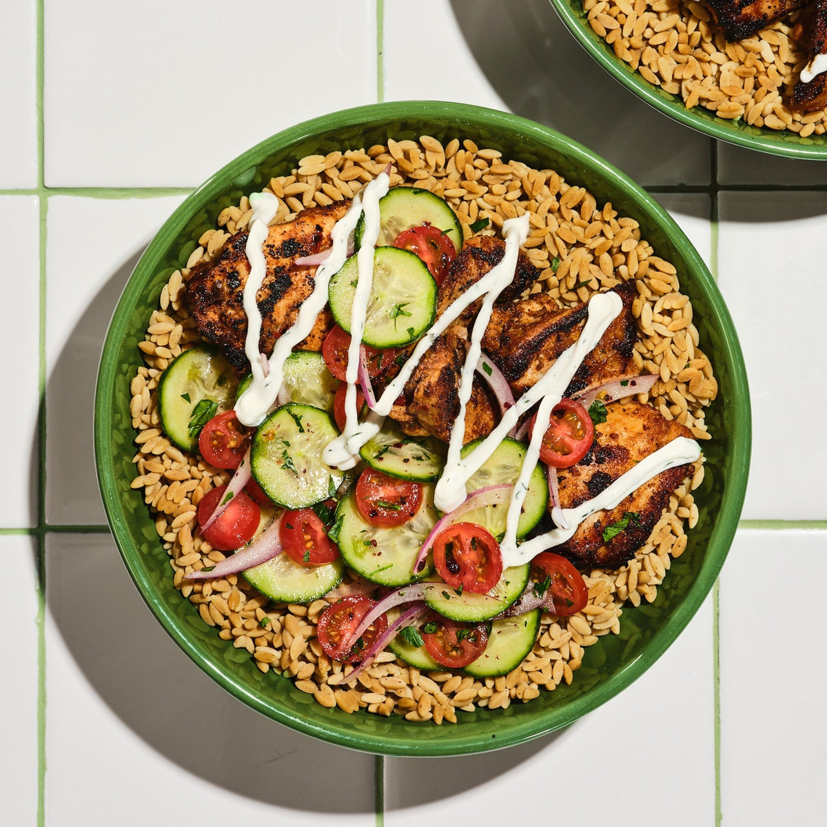 Bowl of Kaizen Protein Rice topped with grilled chicken, cucumber and tomato salad