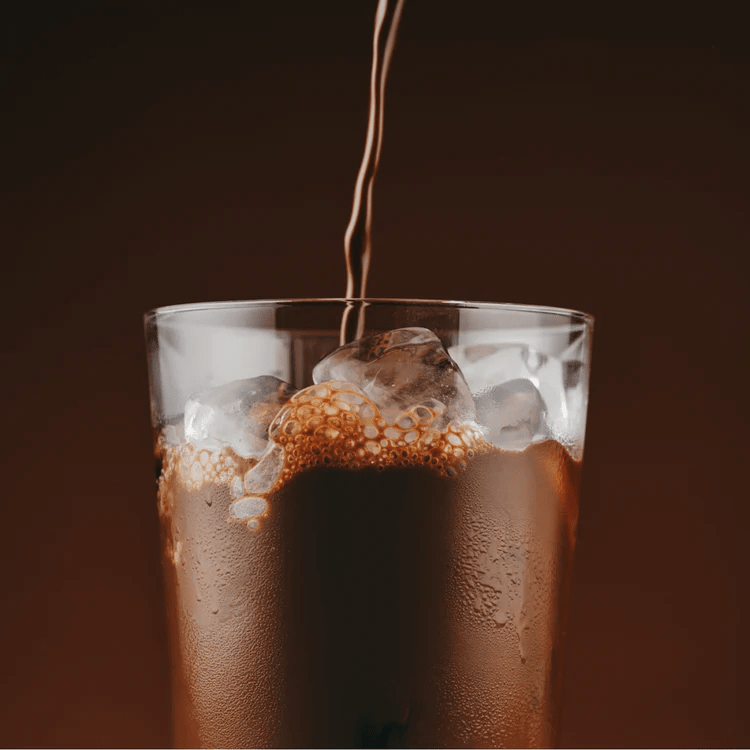 Pouring a chilled chocolate drink over ice in a clear glass, showcasing the refreshing texture of Sodii's Salty Chocolate - 30 Serve Tub for keto and low carb fans.