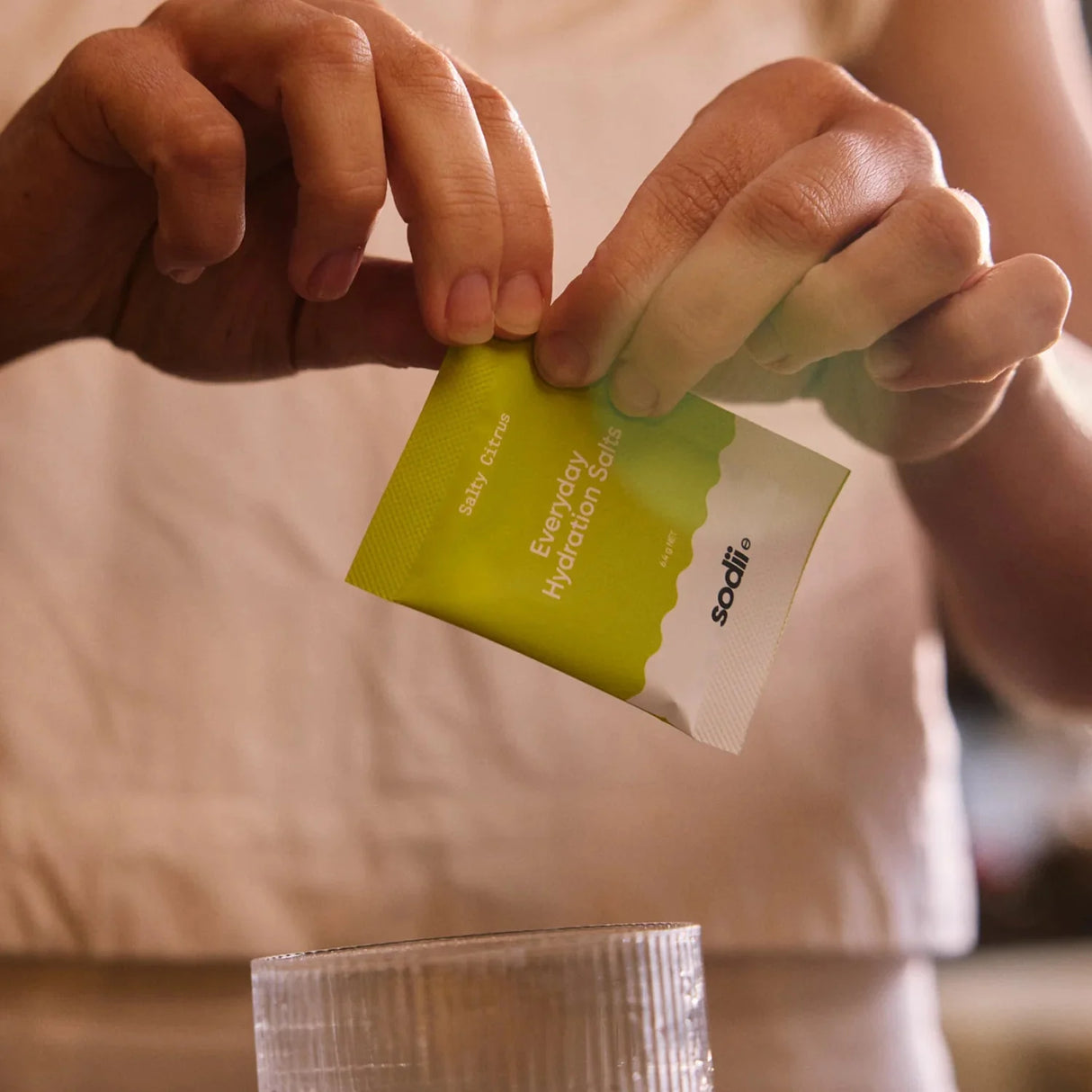 Person holding a Salty Citrus - 30 Sachets electrolyte packet by Sodii preparing a drink in a clear glass
