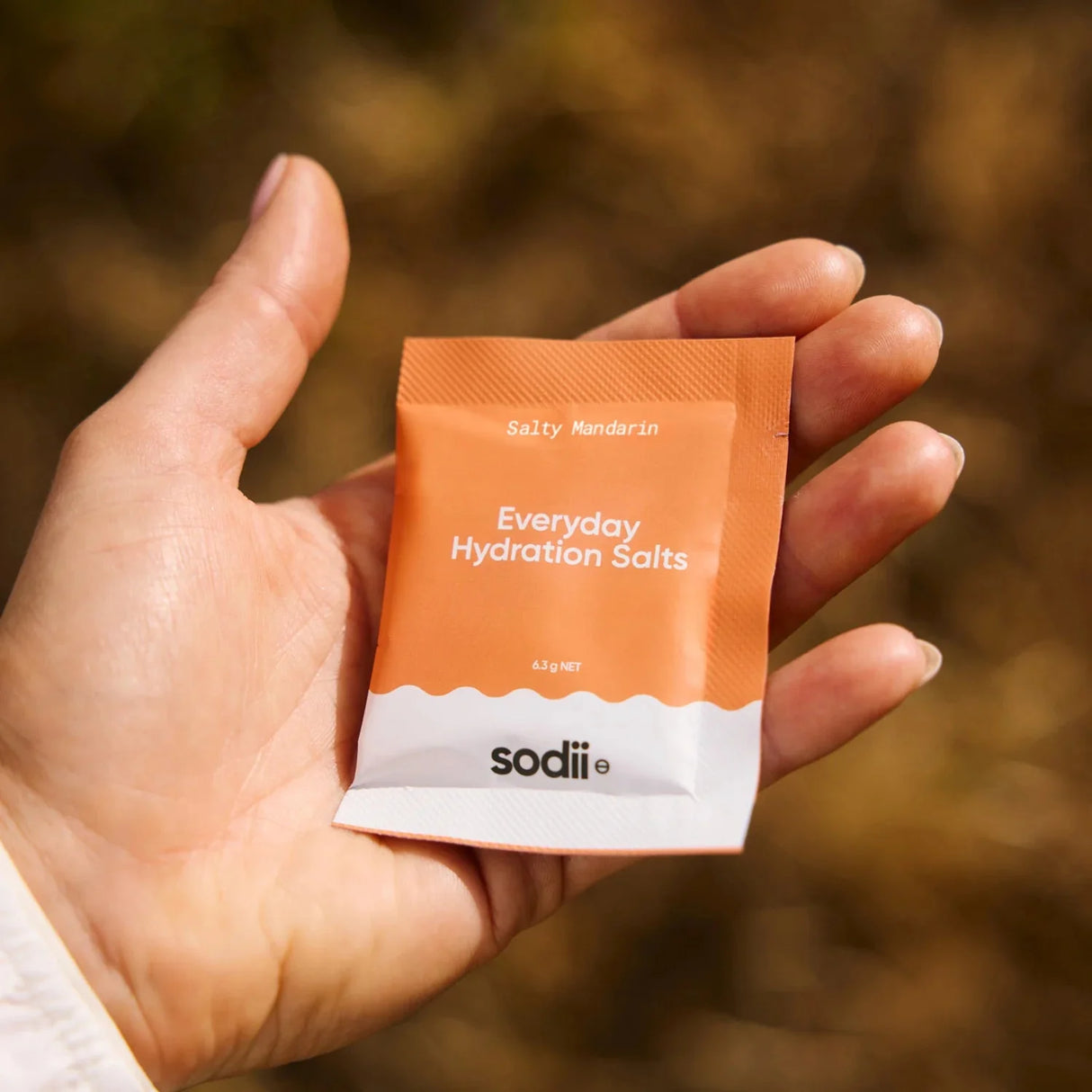 Hand holding a single orange and white sachet of Salty Mandarin - 30 Sachets by Sodii from the Electrolytes collection