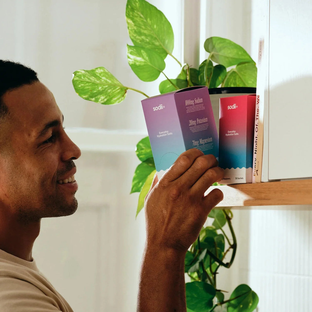 Man taking Salty Passionfruit - 30 Sachets by Sodii from kitchen shelf with green plant in background
