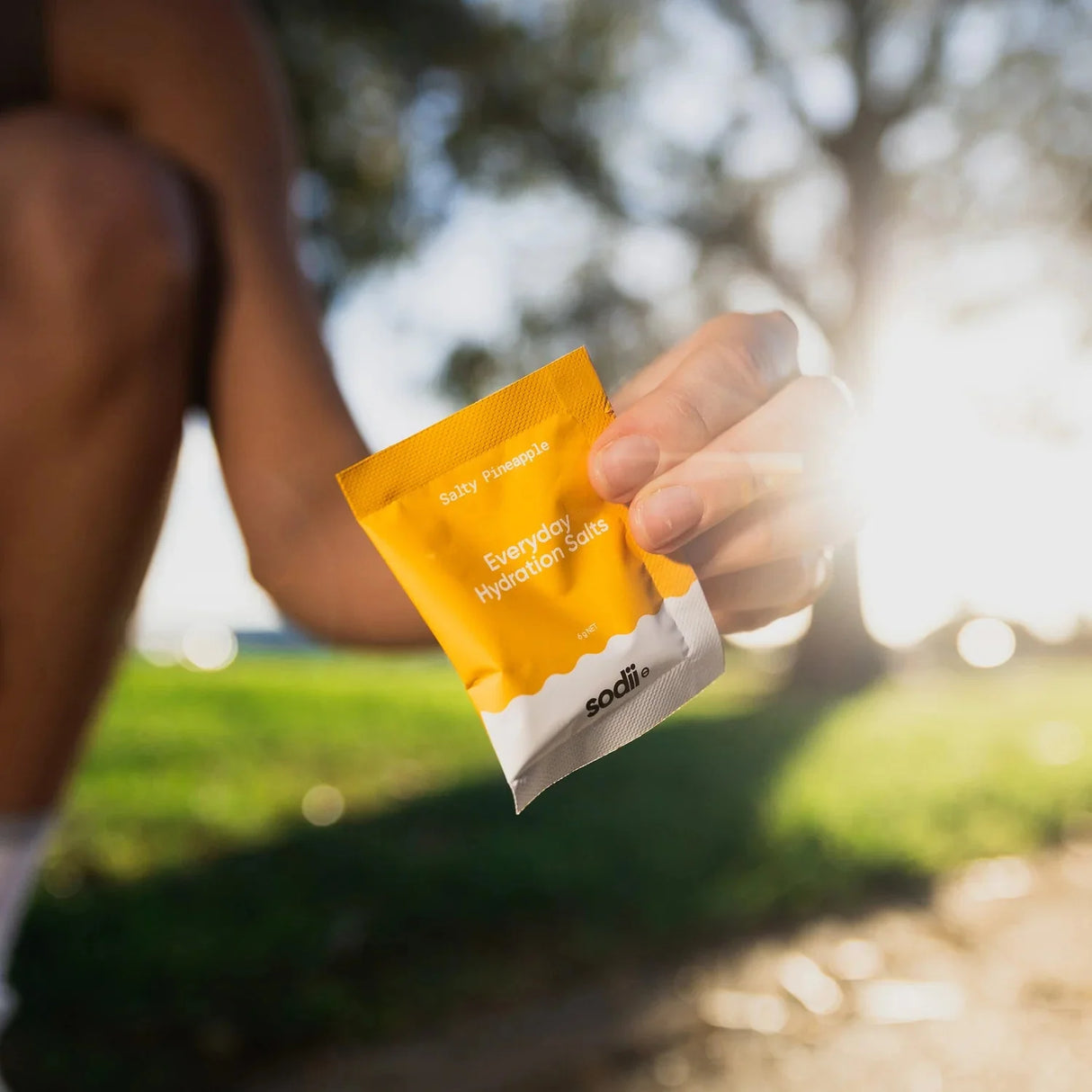 Hand holding a bright yellow sachet of Salty Pineapple - 30 Sachets by Sodii outdoors with blurred background.