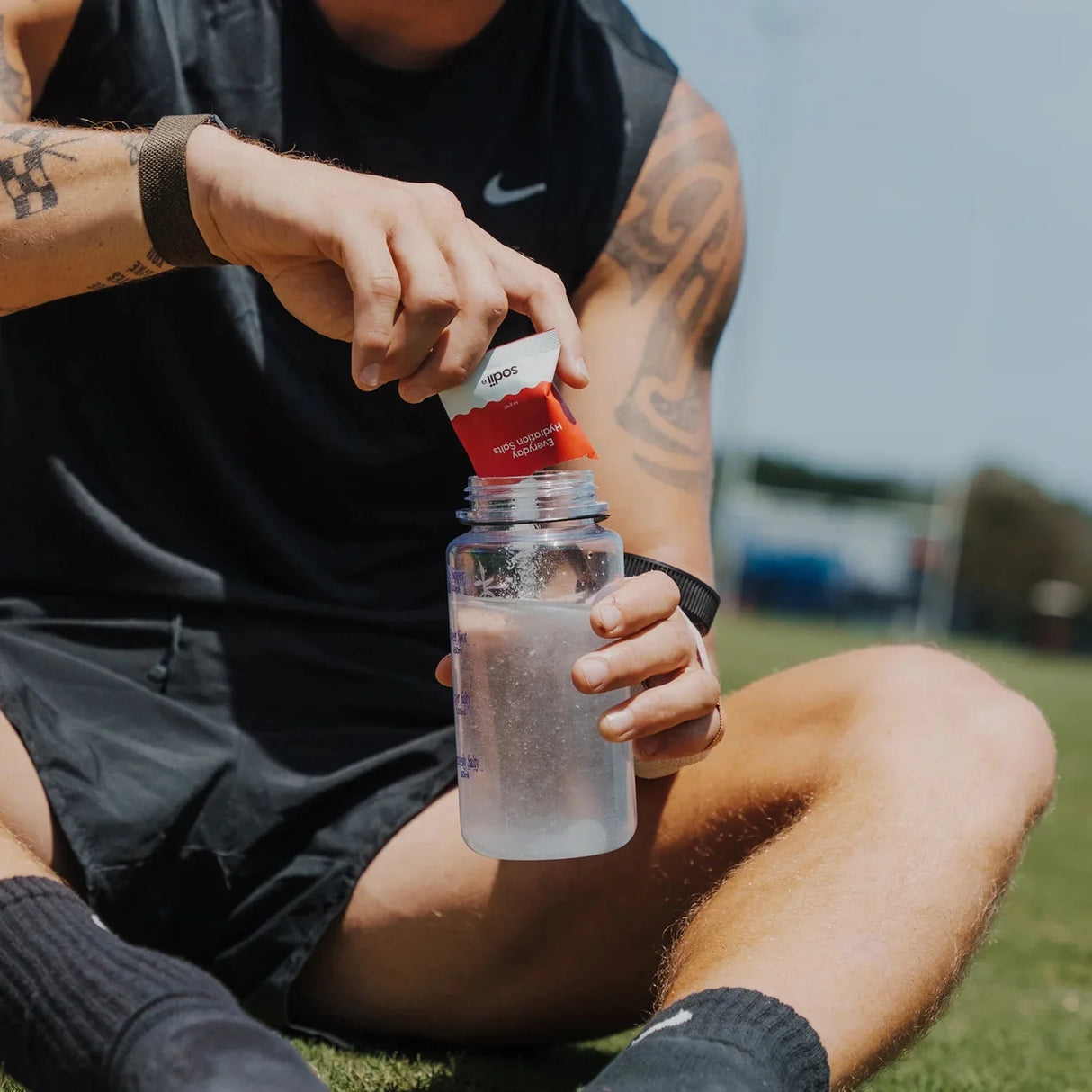 Man adding Salty Raspberry - 30 Sachets electrolyte drink by Sodii to water bottle outdoors on sports field
