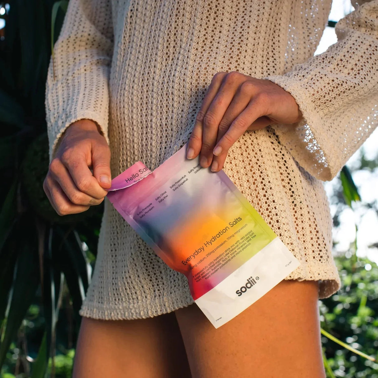 Person holding Salty Variety Pack - 8 Sachets by Sodii, featuring colorful hydration salts pouch with nature background.