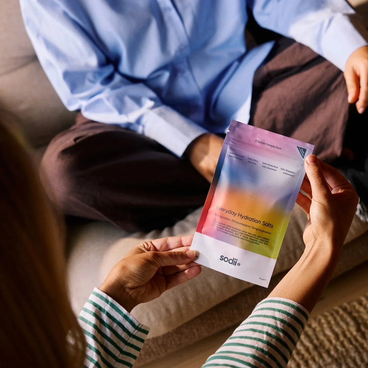 Person holding Sodii Salty Variety Pack - 8 Sachets hydration salts with another person seated nearby indoors