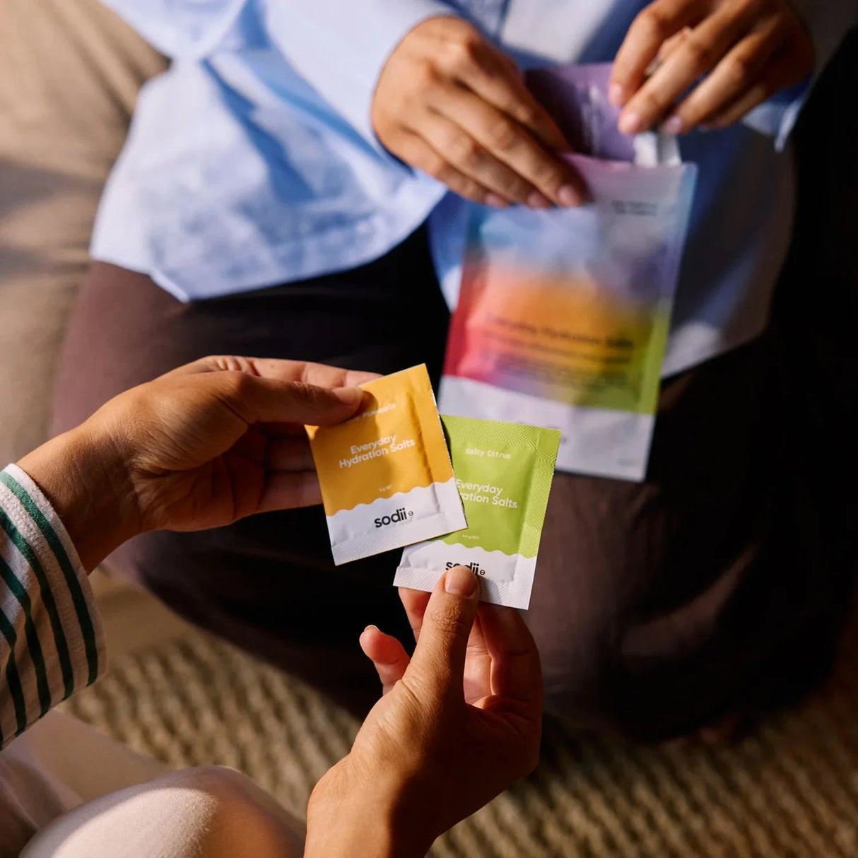 Salty Variety Pack - 8 Sachets by Sodii held by two people with colorful sachets and pouch in casual indoor setting