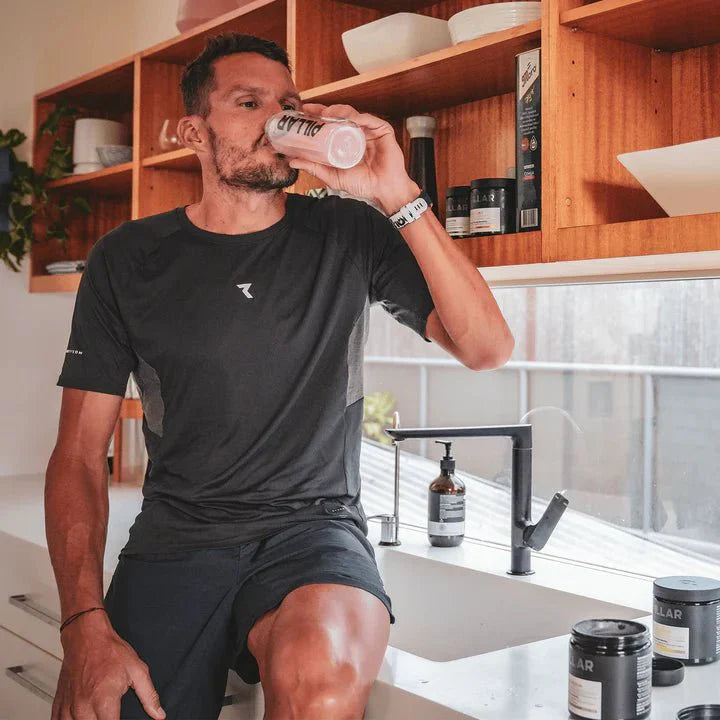 Man in black activewear drinking from branded shaker in kitchen with Triple Magnesium Powder - Lemon Lime - 200g jars nearby