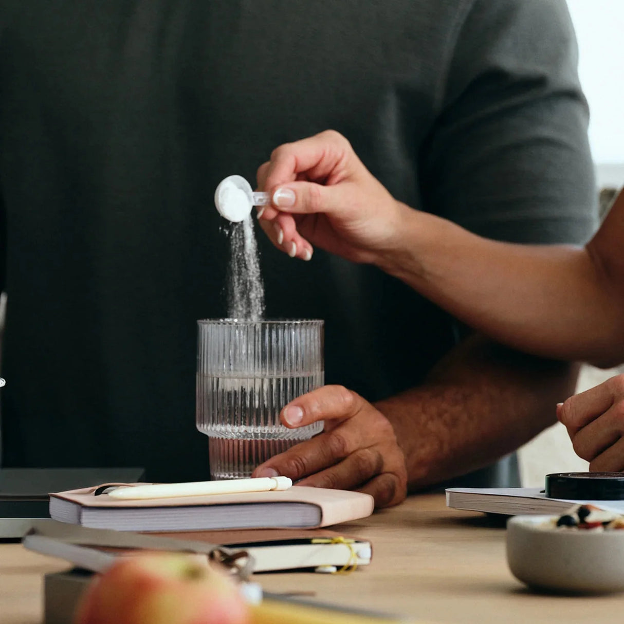 Person pouring powder from a scoop into a glass of water for Unflavoured - 30 Sachets by Sodii in a work setting