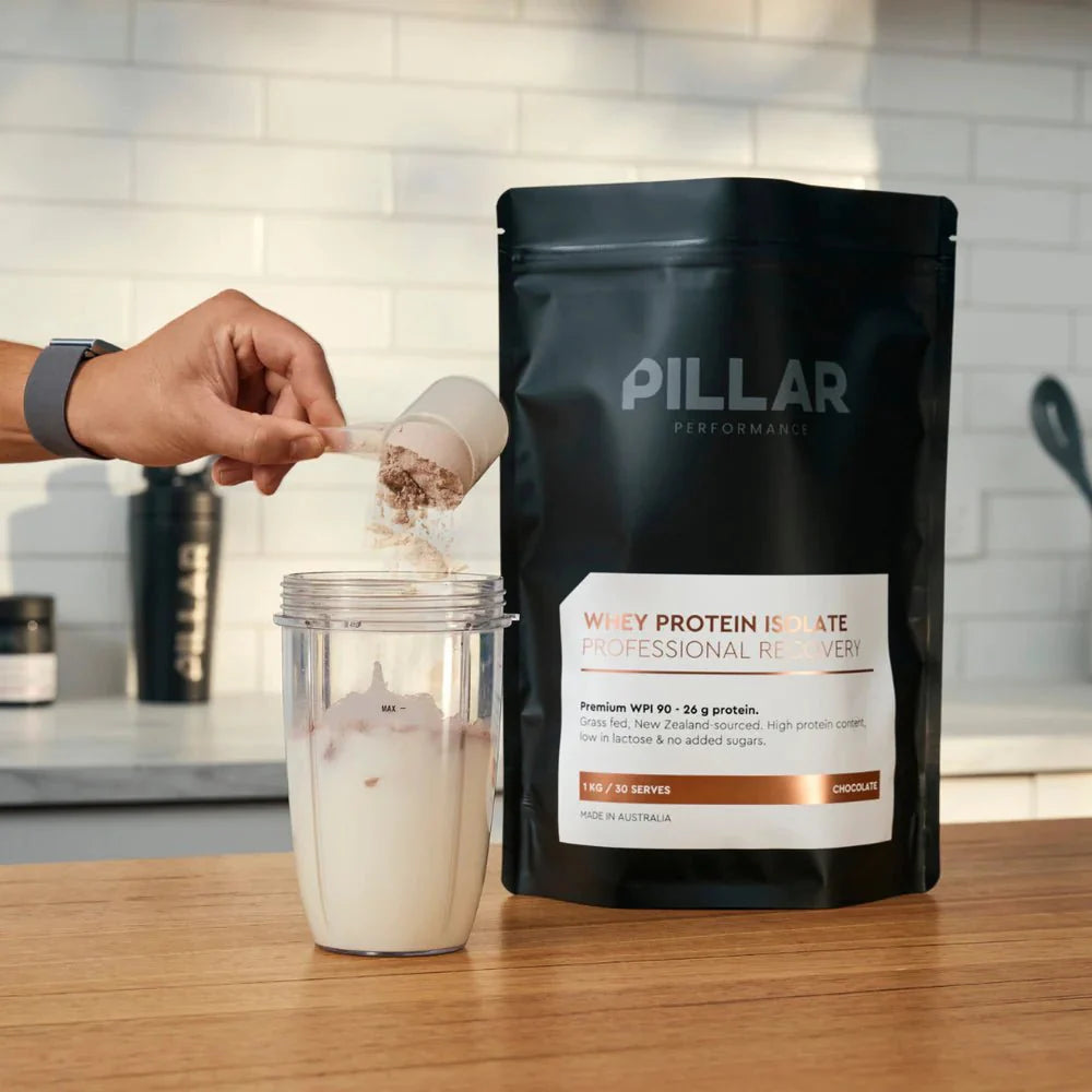 WPI - Vanilla - 1kg by PILLAR PERFORMANCE in black resealable pouch with scoop measuring protein powder over milk shaker