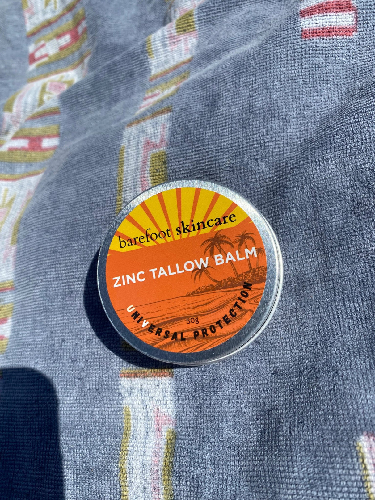 Zinc Tallow Balm - 130g in small round tin with orange label by Barefoot Skincare Co on blue fabric background