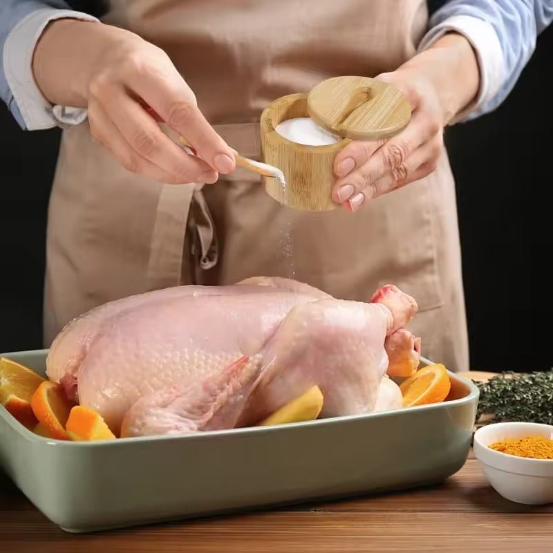 Person seasoning raw whole chicken with Bamboo Salt Box wooden container by Salt Cellar, kitchen spices setting