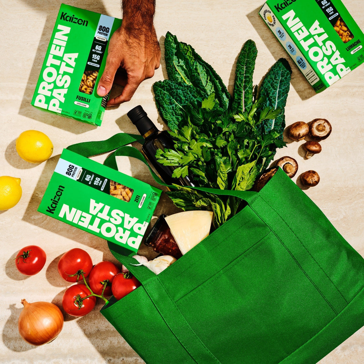 Kaizen Protein Pasta boxes in a green shopping bag with fresh vegetables