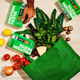 Kaizen Protein Pasta boxes in a green shopping bag with fresh vegetables