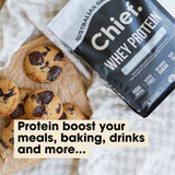 Grass-fed Whey Protein Powder - Creamy Vanilla - 900g by Chief beside freshly baked chocolate chip cookies on parchment paper